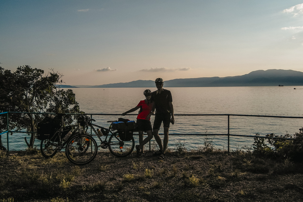 fotka dvojice bicyklistov v pozadí s chorvátskym morom a západom slnka